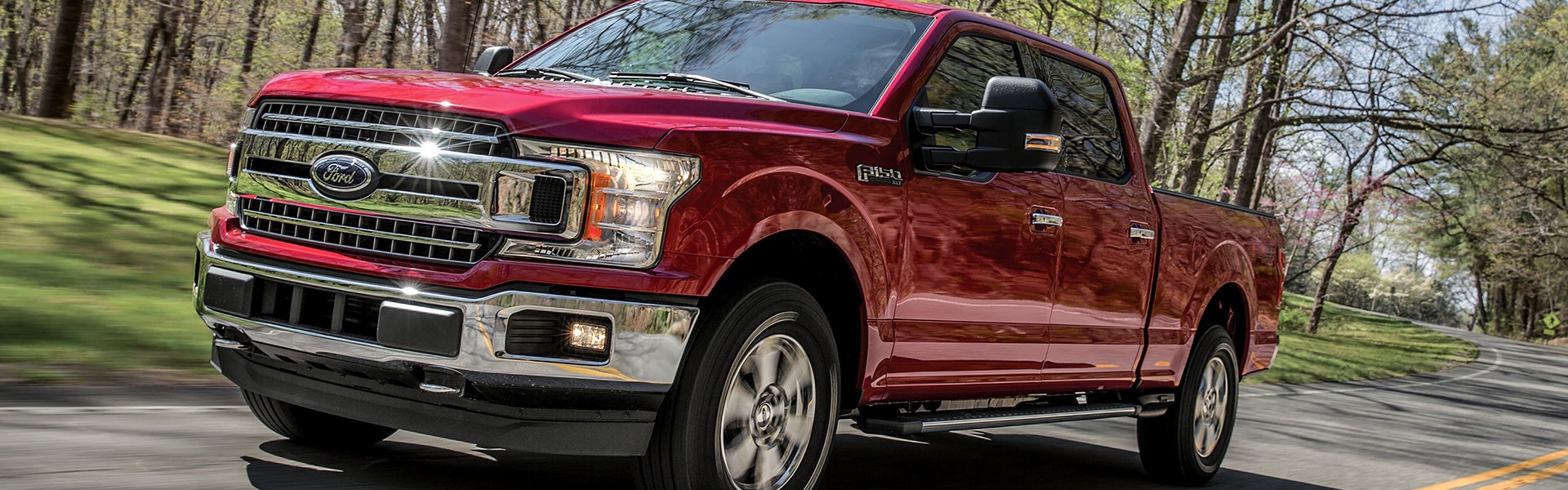 Red Ford F-150 pickup truck driving on a paved road through trees