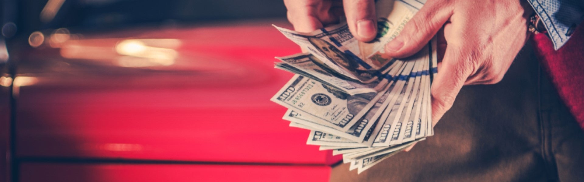 Person holding a stack of cash beside a red car