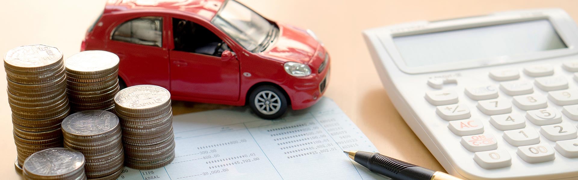 Small red toy car next to stacked coins, a calculator, and a pen
